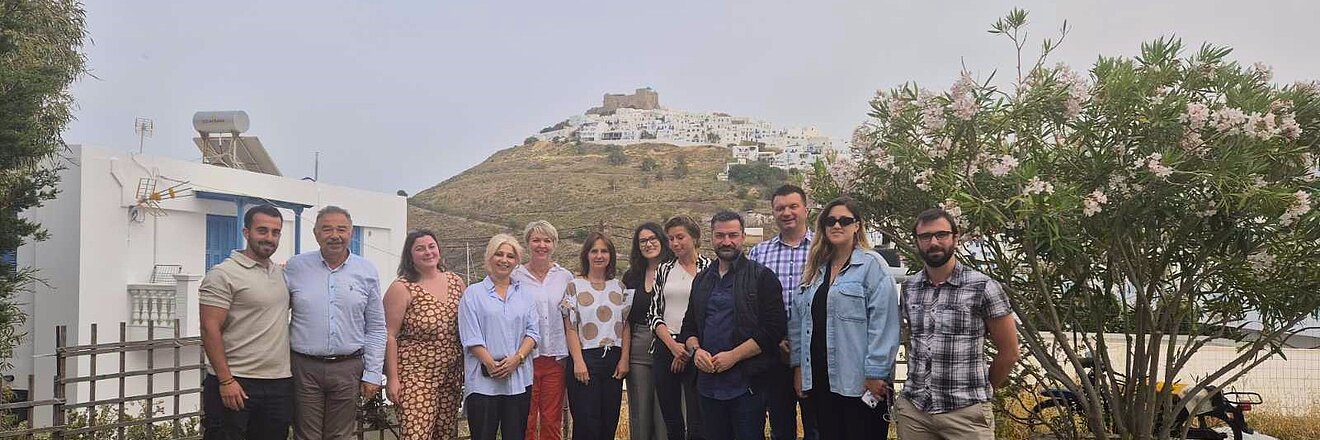 Group photo of 12 people attending a seminar on Greek island Astypalea with the old town of Astypalea in the background of the image.