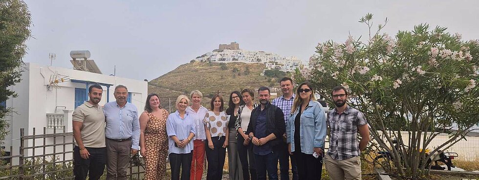 Group photo of 12 people attending a seminar on Greek island Astypalea with the old town of Astypalea in the background of the image.