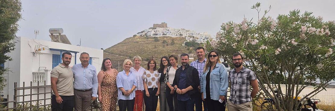 Group photo of 12 people attending a seminar on Greek island Astypalea with the old town of Astypalea in the background of the image.