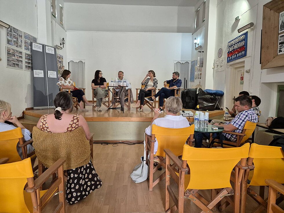 Seminar image with five people on stage holding a panel discussion and several persons in the audience.