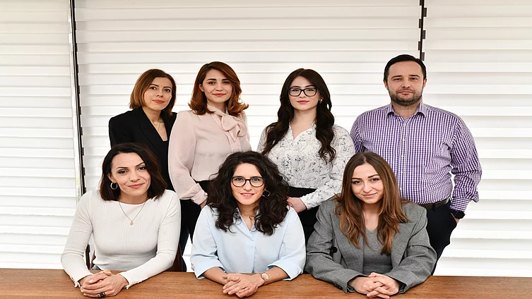 Seven members of the FES Dialogue Southeast Europe project team pose for a formal group photo in front of white blinds. In the back row, from left to right, stand Selma Šehović, Saša Vasić, Ema-Džejna Smolo-Zukan, and Harun Cero. In the front row, seated at a wooden table from left to right, are Lejla Garaplija, Sarah Hees-Kalyani, and Jasmina Pirija.